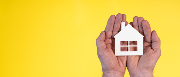 Έννοια της ασφάλισης στο σπίτι με χάρτινο σπίτι στα χέρια σε κίτρινο φόντο - Φωτογραφία, εικόνα