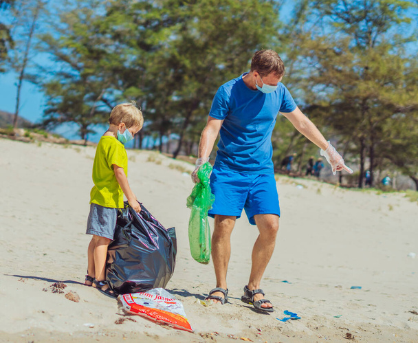 Volunteer blue face mask forest sand beach. Son helps father hold black bag for pick up garbage. Problem spilled rubbish trash planet pollution environmental protection. Natural children education - Foto, afbeelding