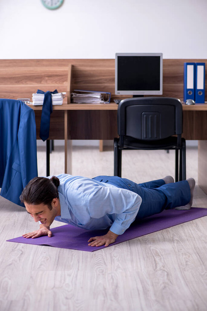 Young handsome businessman doing exercises at workplace - Fotoğraf, Görsel