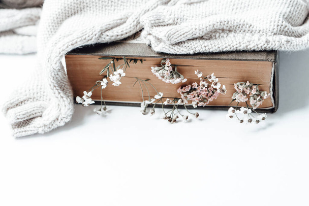Libro viejo con flores de campo como marcadores y suéter cálido. Foto: - Foto, imagen