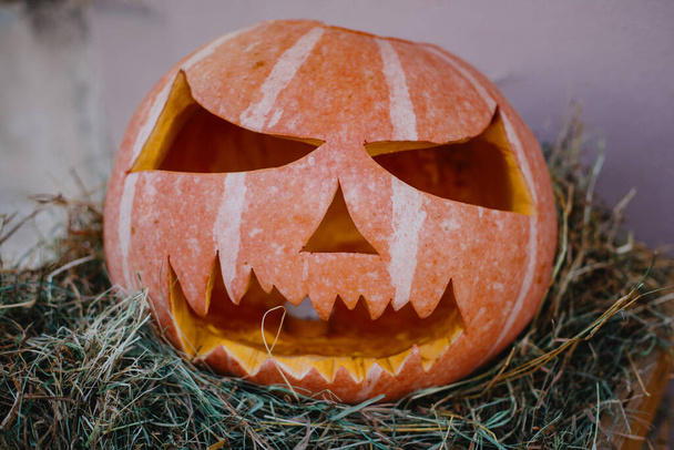 Carved pumpkin with scary face on hay bale, modern festive decoration of european street. Happy Halloween. Halloween street decor. - Photo, Image
