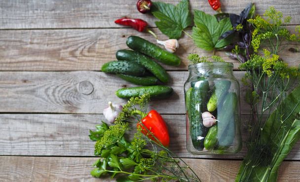 The benefits and harms of canned cucumbers. The process of home canning cucumbers in glass jars under lids for storage for the winter. Jars of cucumbers on a wooden background with ingredients for preservation. - Photo, Image