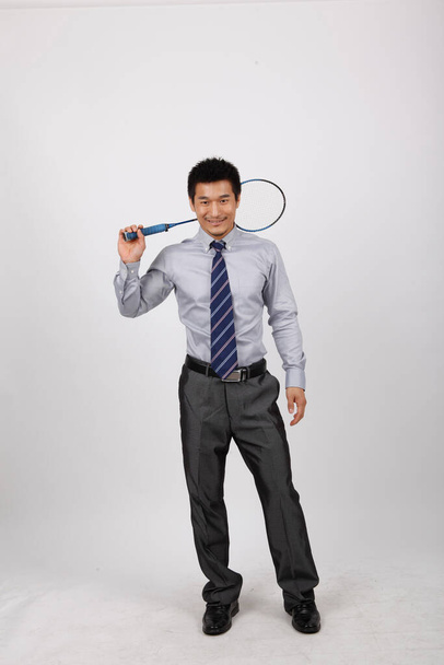 A young man playing badminton in business clothes - Фото, изображение