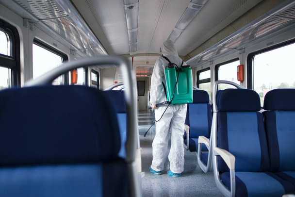 公共交通機関医療。感染性の高いコロナウイルスやCOVID-19の拡散を停止するには、地下鉄の列車の内部を消毒し、消毒白い保護スーツの男. - 写真・画像