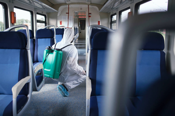 Salud en transporte público. Hombre en traje de protección blanca desinfectando y desinfectando el interior del tren subterráneo para detener la propagación del coronavirus altamente contagioso o COVID-19. - Foto, imagen