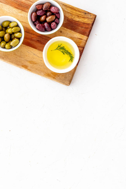 Olives and olive oil in bowls on cutting board on white top view copy space - Foto, Imagen