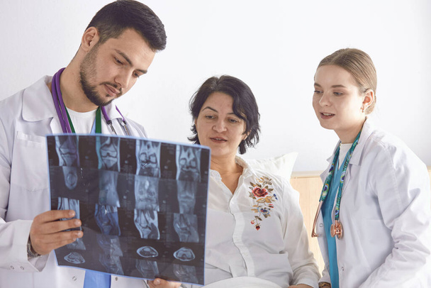 Доктор смотрит рентгеновские снимки пожилой женщины
 - Фото, изображение