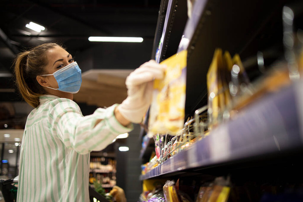 Lebensmitteleinkauf während der COVID-19-Pandemie. Frau mit Maske und Handschuhen kauft Lebensmittel im Supermarkt. - Foto, Bild