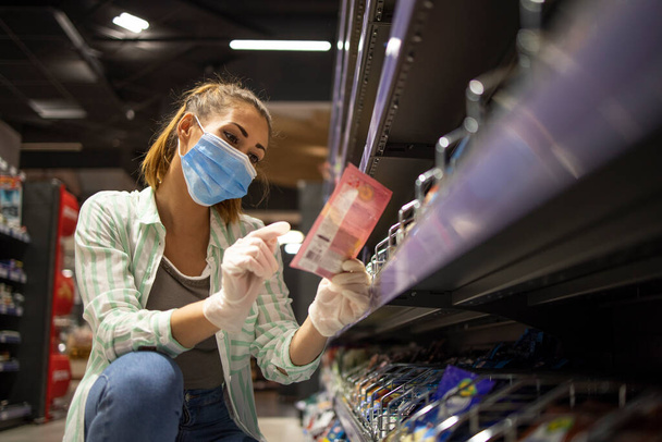 Lebensmitteleinkauf während der COVID-19-Pandemie. Frau mit Maske und Handschuhen kauft Lebensmittel im Supermarkt. - Foto, Bild