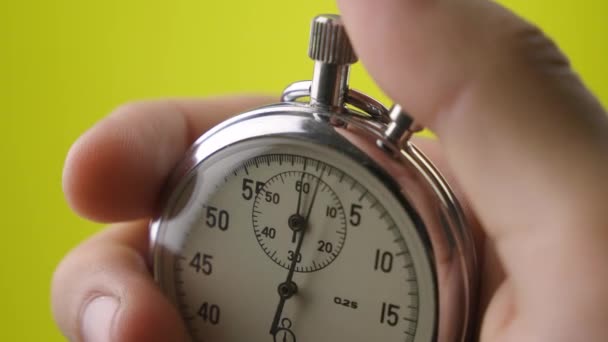 Gros plan chronomètre analogique en mans main sur fond jaune commence et s'arrête - Séquence, vidéo
