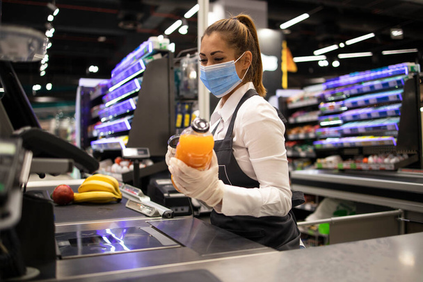 Работает во время пандемии ковида-19. Кассир в супермаркете в маске и перчатках полностью защищен от вируса короны. - Фото, изображение