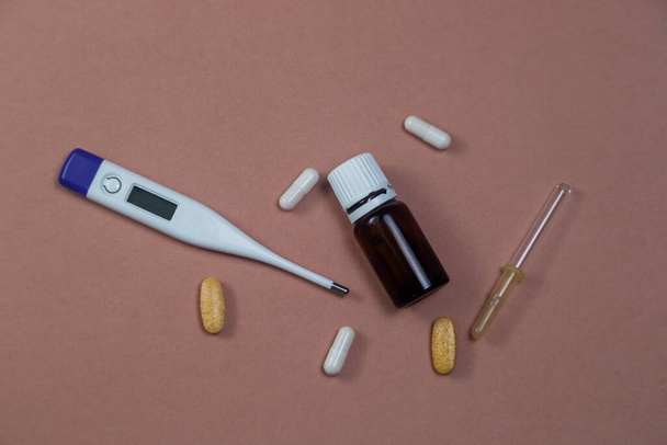 cold season is open. Cold medicines, pills, drops, pipette, thermometer on a solid brown paper background - Valokuva, kuva