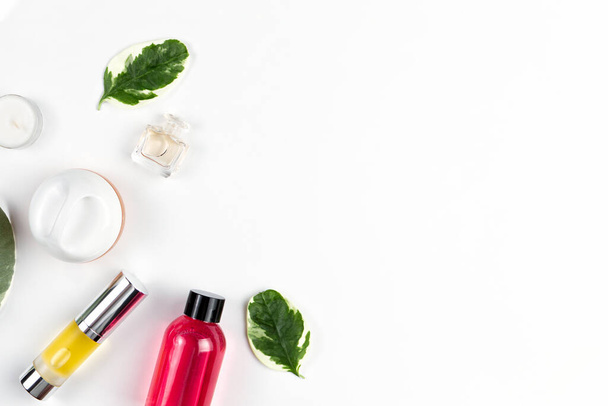 Cosmetics composition. Green leaves, shower gel, perfume, oil in a tube and a candle are laid out on a white background. Copy space. Flat lay. Horizontal. - Photo, Image
