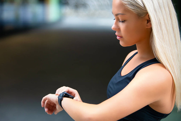 Профиль бегуньи, проверяющей умные часы после тренировки на дороге - Фото, изображение