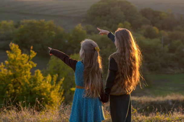 Two little sisters at sunset in the fall in nature. The little sisters are alone. Beautiful long-haired girls and autumn nature - Fotó, kép
