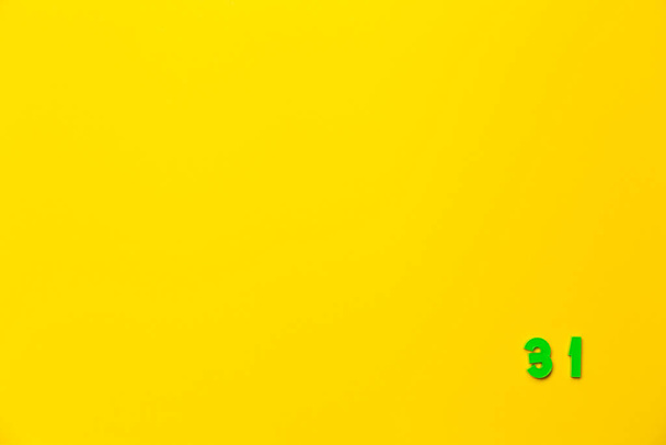Ένα πράσινο πλαστικό παιχνίδι αριθμός τριάντα ένα βρίσκεται στην κάτω δεξιά γωνία σε κίτρινο φόντο. - Φωτογραφία, εικόνα