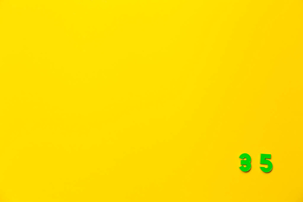 Um brinquedo de plástico verde número trinta e cinco está localizado no canto inferior direito em um fundo amarelo. - Foto, Imagem