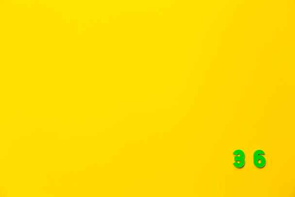 Un juguete de plástico verde número treinta y seis se encuentra en la esquina inferior derecha sobre un fondo amarillo. - Foto, imagen