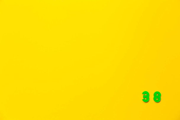 Un giocattolo di plastica verde numero trentotto si trova nell'angolo in basso a destra su uno sfondo giallo. - Foto, immagini