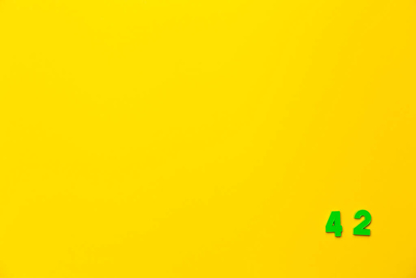 Um número de brinquedo de plástico verde quarenta e dois está localizado no canto inferior direito em um fundo amarelo. - Foto, Imagem