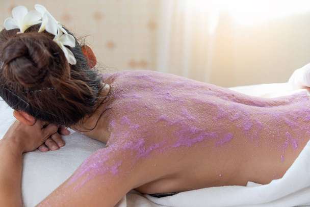 Jonge Aziatische vrouw met scrubben behandeling met body scrub in spa salon, schrobben en huidverzorging concept, genieten en ontspannen tijd - Foto, afbeelding