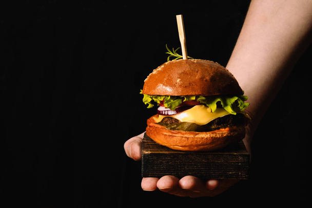  Chefs hand serving fresh burger on black background - 写真・画像