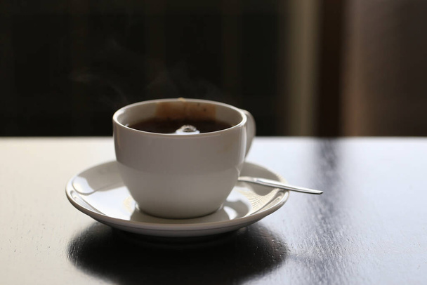 Чайна сумка в чашці з ложкою та соусом. Біла керамічна чашка чаю на дерев'яному столі з темною сценою
 - Фото, зображення
