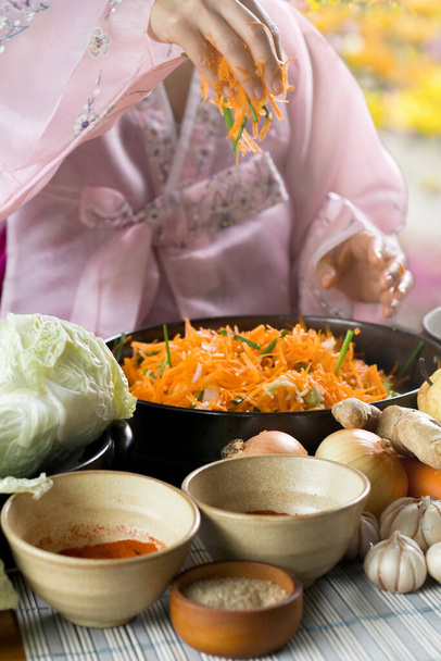 Nahaufnahme einer Frau in traditioneller Kleidung während der Kimchi-Vorbereitung. Koreanische Küche berühmte Beilage, fermentiertes Gemüse, Kohl, Rettich, würzige und duftende Gewürze wie Apfel oder Birne, Zwiebeln, Knoblauch, Ingwer & Frühlingszwiebeln - Foto, Bild