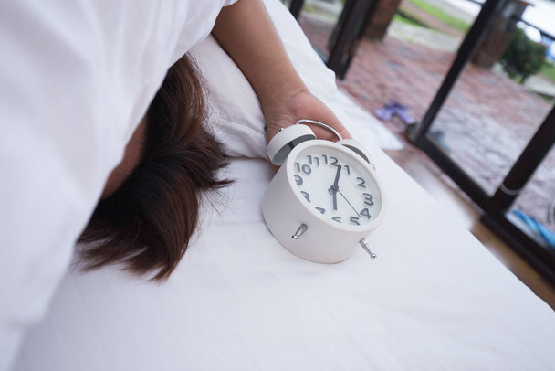 Ο άνθρωπος κοιμάται στο λευκό κρεβάτι με το λευκό ξυπνητήρι το πρωί - Φωτογραφία, εικόνα