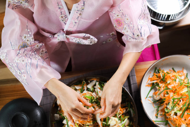 Primer plano de las manos femeninas durante la preparación de Kimchi. Cocina coreana famosa guarnición, verduras fermentadas, col, rábano, condimentos picantes y olorosos incluyendo manzana o pera, cebollas, ajo, jengibre y cebolla de primavera - Foto, imagen