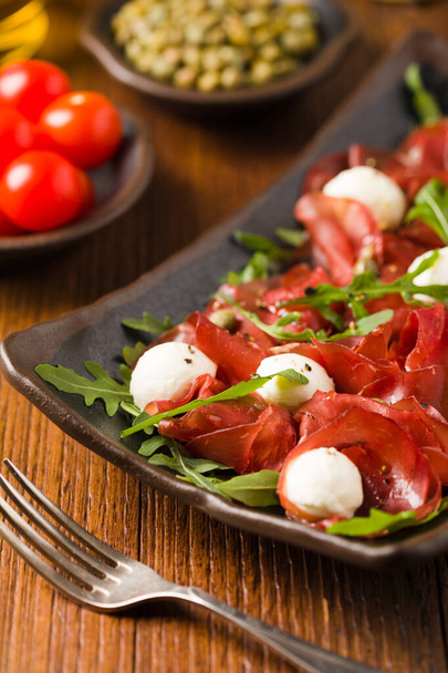 Beef carpaccio served with balls of mozzarella cheese, arugula and capers. Front view. Close-up. - Photo, image