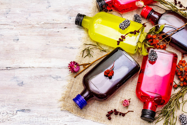 Homemade assortment of berries liqueurs or tincture. Sweet mountain fruits, fragrance herbs, glass bottles. White old wooden boards background, top view - Valokuva, kuva