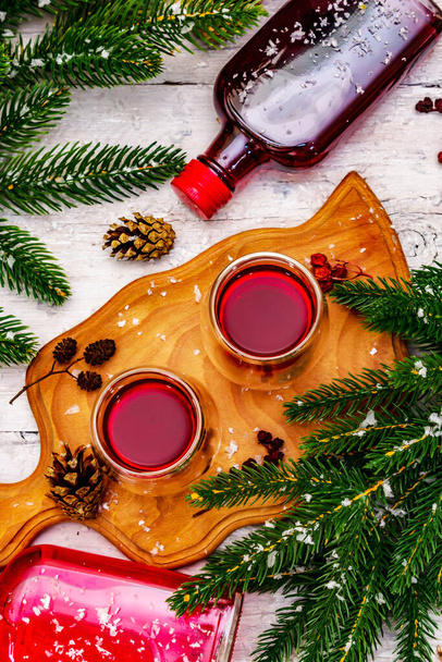 Festive berries liqueur or tincture in double-walled glasses. Ingredient for preparation alcohol cocktail. New Year or Christmas design, white wooden boards background, top view - Photo, Image