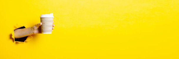 Mano femminile che tiene una tazza di carta di caffè su uno sfondo giallo brillante. Bandiera - Foto, immagini