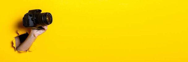 Mano femminile che tiene una macchina fotografica su uno sfondo giallo brillante. Bandiera - Foto, immagini