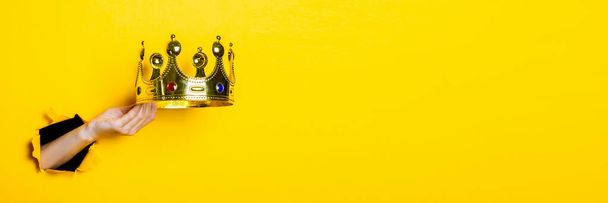 Die weibliche Hand hält eine goldene Krone auf leuchtend gelbem Hintergrund. Banner. - Foto, Bild