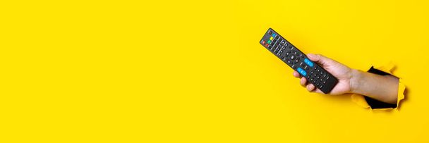 Man's hand holding a TV remote control on a bright yellow background. Banner - Photo, Image