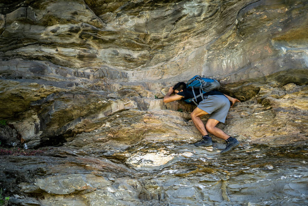 Young boy climbing the rocks wearing a backpack. - 写真・画像