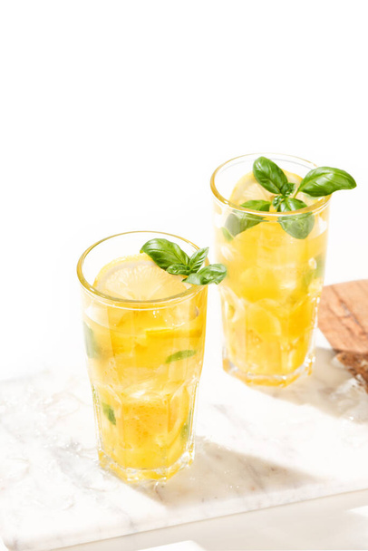 Zitruslimonade oder Mojito-Cocktail mit Zitrone, Orange und Basilikum. Kaltes Getränk oder Getränk mit Eis auf Marmorschneidebrett - Foto, Bild