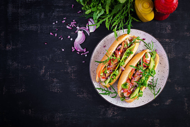 Hot dog with sausage, cucumber, tomato and red onion on dark background. Top view. Flat lay. Copy space - Photo, image