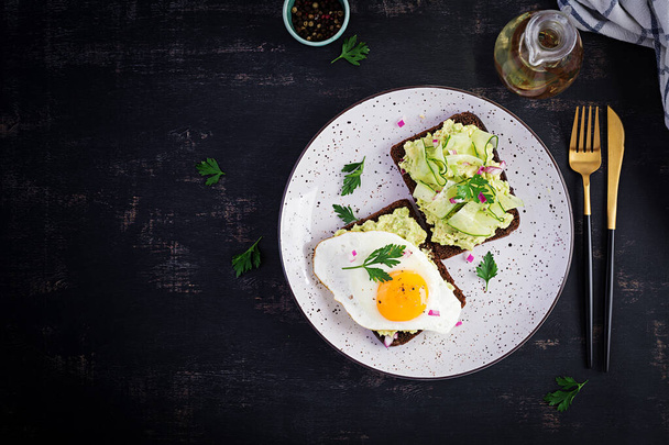 Healthy breakfast. Sandwich with avocado guacamole, cucumber and fried egg,   for healthy breakfast or snack. Top view, overhead, flat lay - Photo, Image