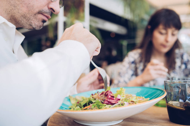 Homme aux cheveux gris mangeant une salade saine avec des amis dans un restaurant. Fille attrayante sur un fond flou - Photo, image