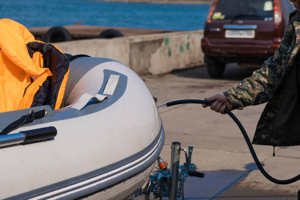 Человек моет лодку из резинового шланга после выхода в море. Капли воды разбросаны с лодки - Фото, изображение