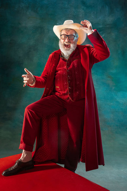 Modern stylish Santa Claus in red fashionable suit and cowboys hat on dark background - Fotó, kép