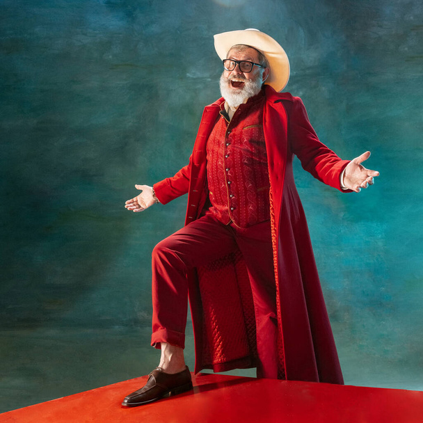 Modern stylish Santa Claus in red fashionable suit and cowboys hat on dark background - Foto, afbeelding