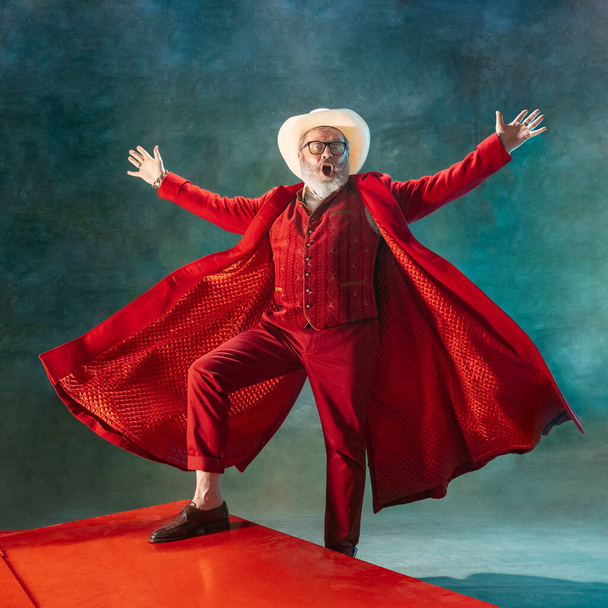 Modern stylish Santa Claus in red fashionable suit and cowboys hat on dark background - Foto, afbeelding