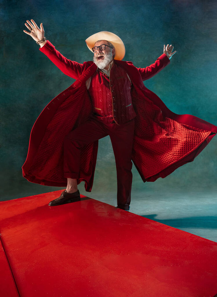 Modern stylish Santa Claus in red fashionable suit and cowboys hat on dark background - Fotografie, Obrázek