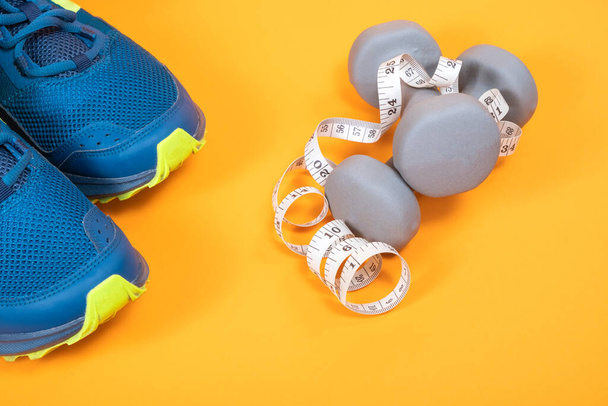 Mancuernas de fitness y cinta métrica y los zapatos deportivos de fitness, equipos deportivos, estilo de vida saludable sobre fondo naranja - Foto, imagen