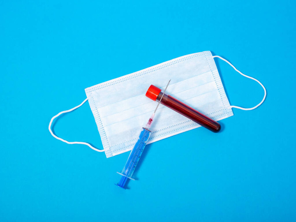 New coronavirus blood test(2019-nCoV), medical face mask, syringe and needle, test tube coronavirus blood test on blue background - Photo, image