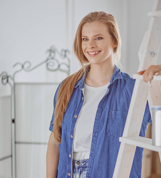 Beautiful young woman on a white wooden stepladder. Ready to repair the room. Women housework concept - Фото, изображение